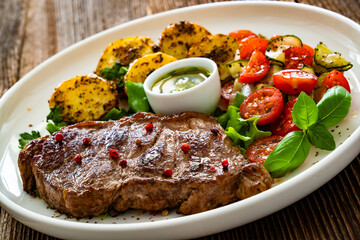 Grilled beef steak with baked potatoes and fresh salad on wooden table	