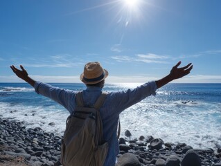 Man back turned arms outstretched at ocean wearing hat  backpack sunny day