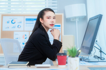 Attractive Asian woman in a formal black suit works attentively at her desk, writing notes. She...