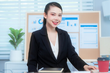 Attractive Asian woman in a formal black suit works attentively at her desk, writing notes. She...