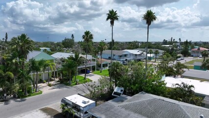 American flag of house in luxury city of Indian Rocks Beach with long palm trees. Aerial approaching shot. Villas, apartments and homes in small town of Florida. Clouds at sky. - Powered by Adobe