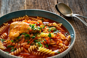 Tomato soup with chicken thigh and noodles on wooden table