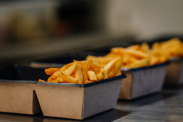 Golden, crispy French fries served in cardboard trays, lined up on a counter, ready for takeaway at...