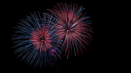 Colorful fireworks display with red and blue explosions illuminated against a black background