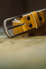 This stylish yellow leather belt with a sturdy metal buckle elegantly rests on a rustic surface. It...