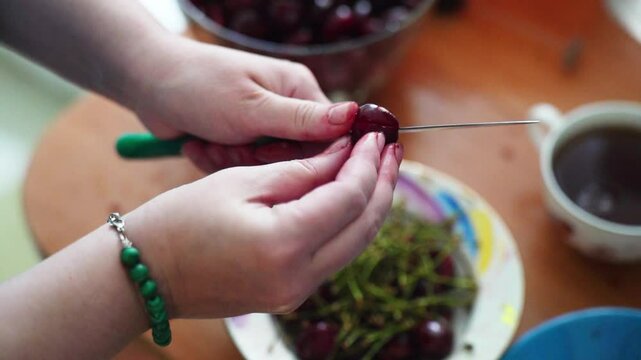 Slow-motion close-up of a woman's hands removing pits from ripe red cherries using a knife, showcasing meticulous fruit preparation
