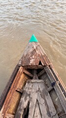 A weathered wooden boat pierces murky river water, its green bow contrasting against the textured...