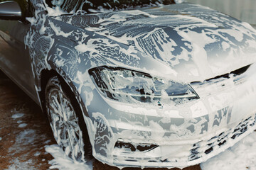 A shiny silver car is getting a thorough soap foam wash in a clean and wellmaintained service area,...