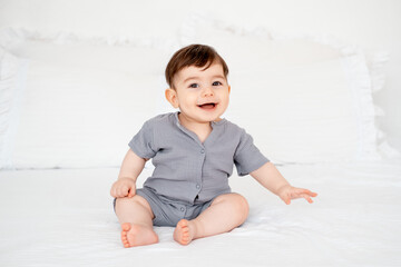 smiling baby on a white bed after sleeping, cute baby in a gray cotton bodysuit on a bed, space for...