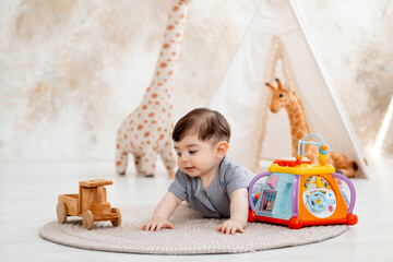 a smiling baby plays in a children's room with soft toys and a teepee, and a cute baby in a gray...