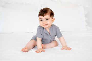 smiling baby on a white bed after sleeping, cute baby in a gray cotton bodysuit on a bed, space for...