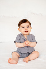 smiling baby on a white bed after sleeping, cute baby in a gray cotton bodysuit on a bed, space for...