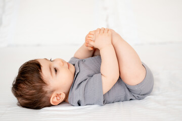 a smiling baby on a white bed after sleeping, a cute baby in a gray cotton bodysuit on a bed, space...