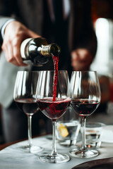 Close up a waiter hand pouring red wine in glasses for wine on the table in restaurant