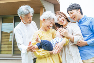 住宅の前で笑顔で赤ちゃんを囲む三世代家族