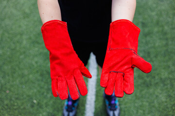 Vibrant and striking red gloves are poised and ready for action on lush green turf, highlighting...