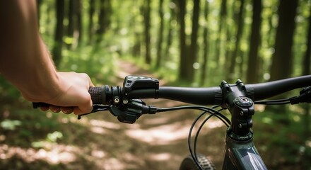 Fototapeta premium Mountain biker's hand grips handlebar during a woodland adventure, exploring the forest path on a sunny day riding the cycle.