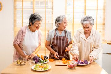 Group of Happy Asian senior woman having dinner eating healthy food together at home. Elderly women friends enjoy indoor lifestyle preparing and cooking vegan food vegetables salad in the kitchen.
