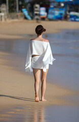 A woman is walking on the beach wearing a white dress