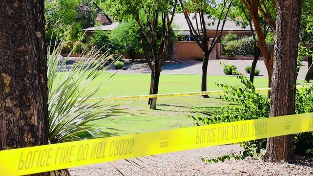 Yellow "POLICE LINE DO NOT CROSS" tape stretches across a sunny outdoor scene at Falcon Field Park