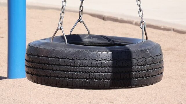 Traditional black tire swing hanging from metal chains over sunlit sand at Falcon Field Park