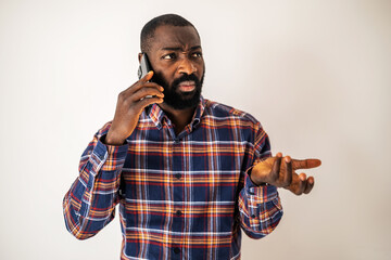 Anxious black man in cozy shirt standing in front of wall and talking on mobile phone.