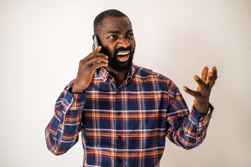 Angry black man in cozy shirt standing in front of wall and talking on mobile phone.