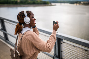 Happy young black woman is enjoying sunny day outdoor and listening music while taking photos.