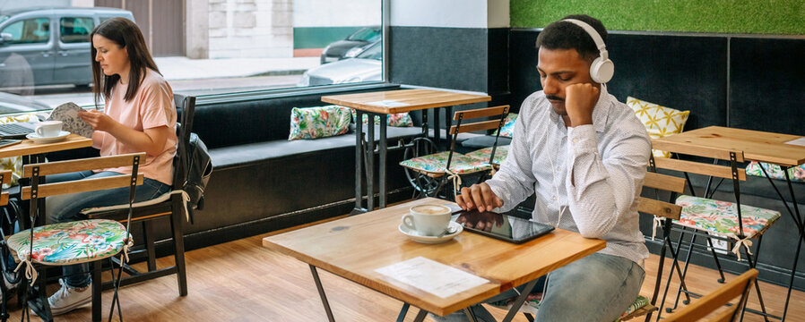 Banner of freelancers working at various tables, engaging with their devices and sipping coffee in a modern cafe featuring large windows, embodying urban life and creativity