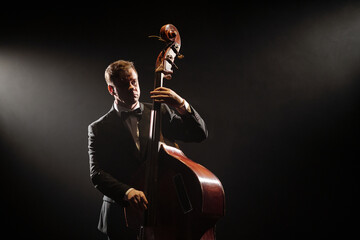 Caucasian middle aged man playing double bass on stage, wearing formal suit, focusing on...
