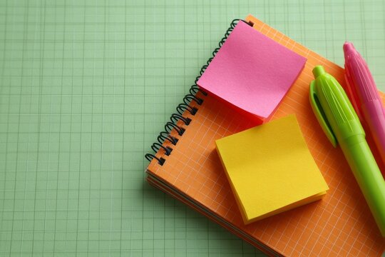 Colorful sticky notes and pens on spiral notebooks over green background