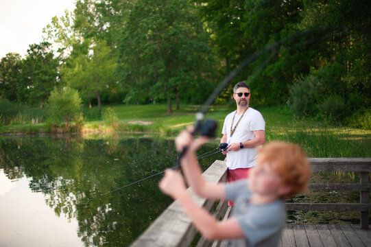 Boy casting fishing line as father watches with pride