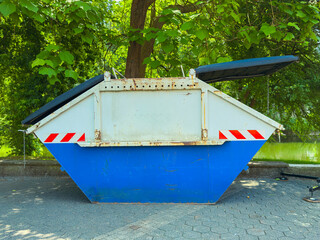 An Industrial Waste Dumpster, which is effectively surrounded by lush and vibrant greenery, serves...