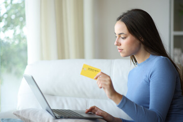 Serious woman using card to pay online with laptop