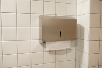 Stainless steel paper towel dispenser mounted on tiled wall in public restroom or washroom. Hygiene...