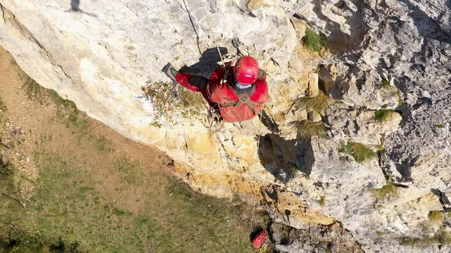  Aerial view of mountain rescuer abseiling on a rocky wall hanging on a rope