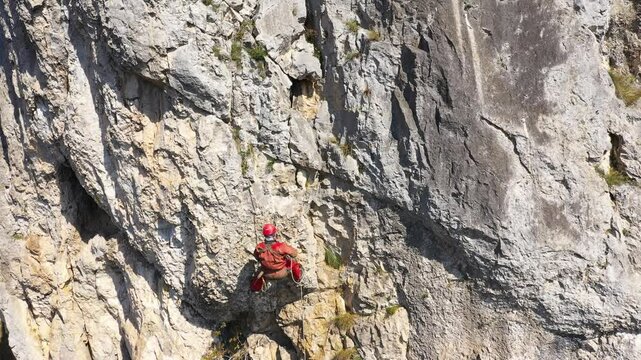  Aerial view of mountain rescuer abseiling on a rocky wall hanging on a rope