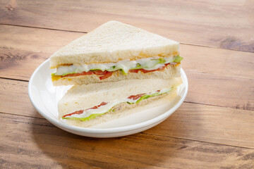 Sandwich with fresh vegetables and creamy salad dressing on white plate isolete on wooden background .