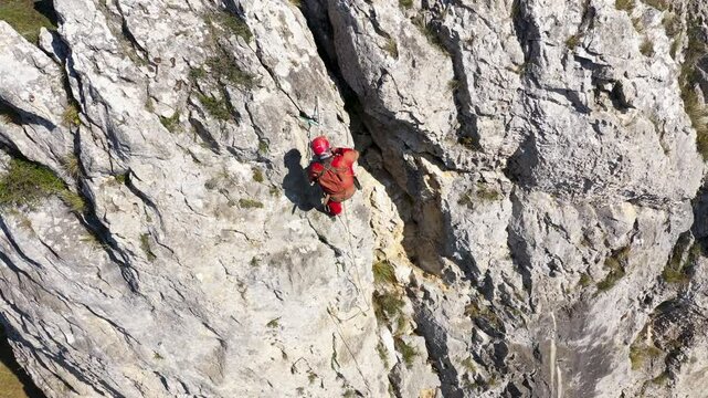  Aerial view of mountain rescuer abseiling on a rocky wall hanging on a rope