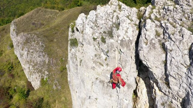  Aerial view of mountain rescuer abseiling on a rocky wall hanging on a rope