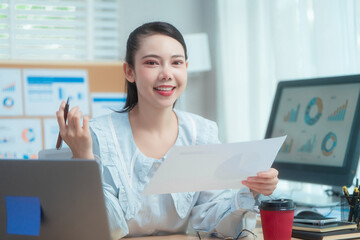 Confident beauty Asian office woman in a formal blouse hard working at her desk, reviewing a...