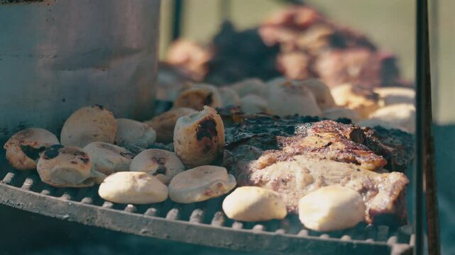 Grilled meat Asado and Chipa, traditional Argentine food with burning and smoking firewood, close up