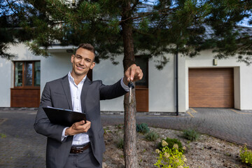 Real estate agent holding keys and clipboard in front of modern house for property