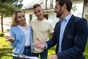 Real estate agent discussing property details with couple using clipboard in front of house