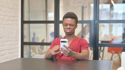 Dissatisfied Young African Man Using Phone in Office