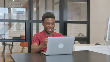 Casual African Man Celebrating Success on Laptop at Workplace
