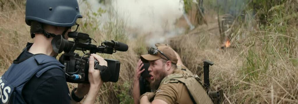 Press interviews soldier in combat zone, shelling starts, soldiers escort journalists through the trench. Concept of war journalism, frontline danger, evacuation.