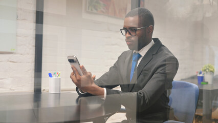 African Businessman Browsing Internet on Phone at Workspace
