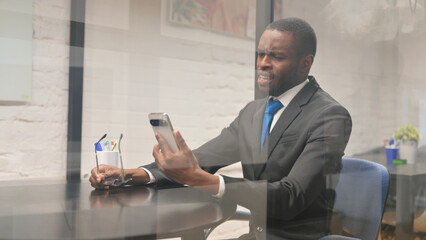African Businessman with Trading Loss on Phone at Workspace