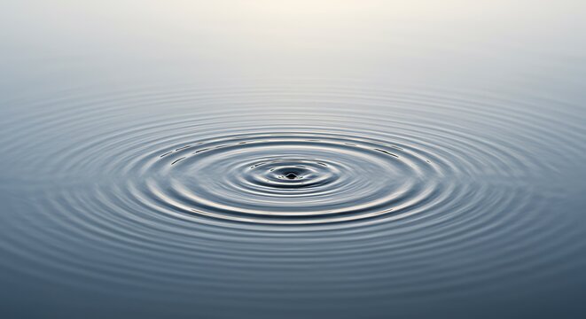 A single water droplet creates concentric ripples on a calm, still surface.
